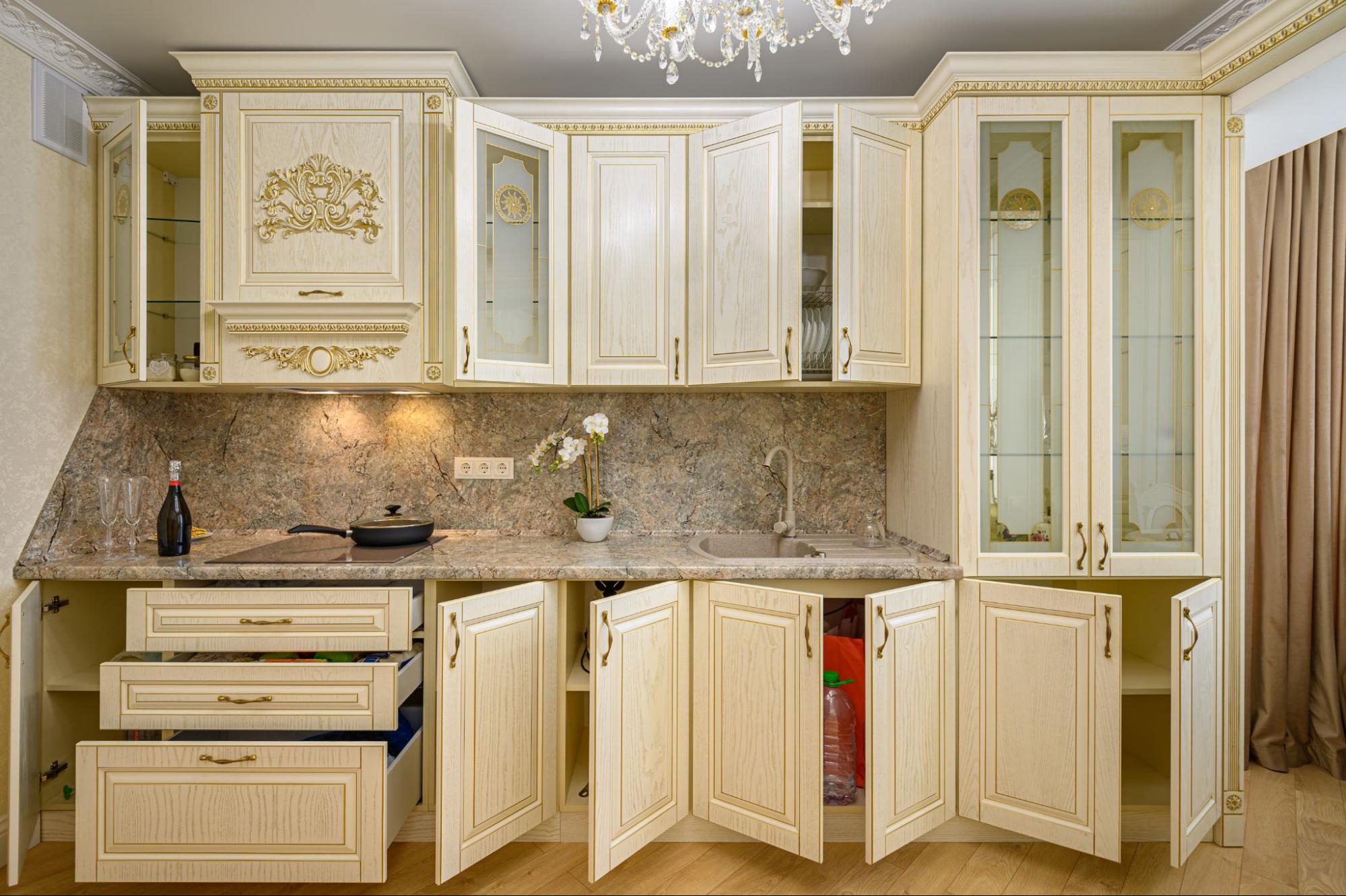 A modern neoclassical beige kitchen with open Shaker-style cabinets, intricate detailing, and glass-front doors.