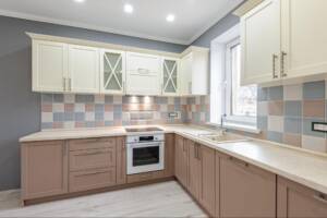 Luxury modern Provence-style kitchen with grey, pink, and cream cabinets and tiled backsplash.