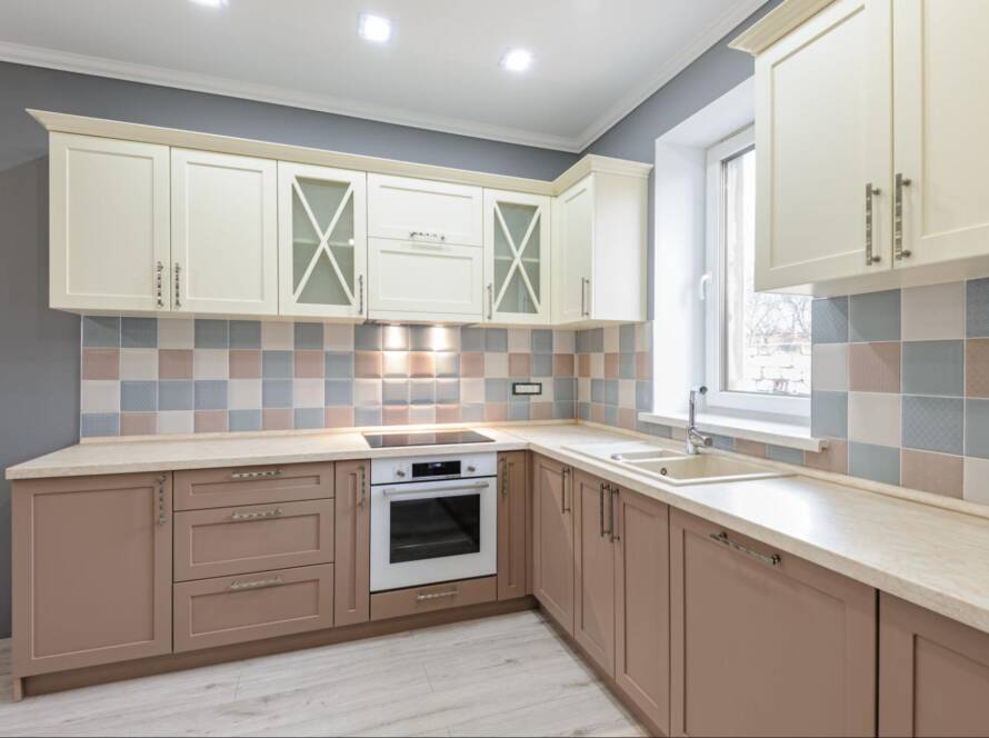 Luxury modern Provence-style kitchen with grey, pink, and cream cabinets and tiled backsplash.